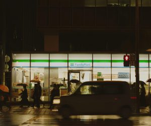 People crossing a street near a FamilyMart in Japan during a rainy night.